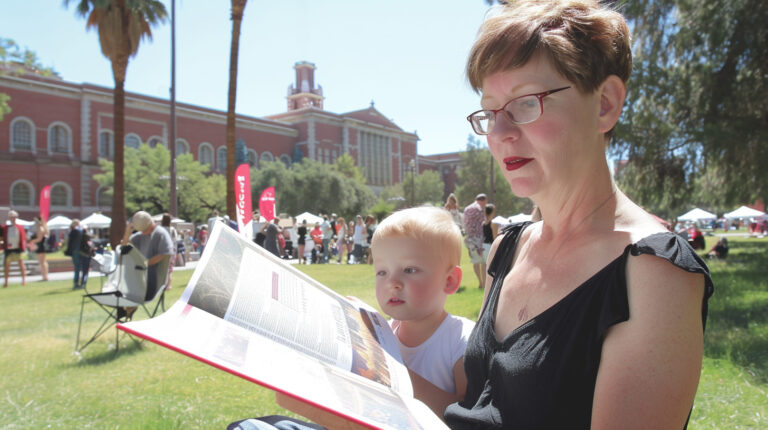 Woman and child enjoying a book on a park bench at the Tucson Festival of Books, embodying the joy of shared reading in a community setting.